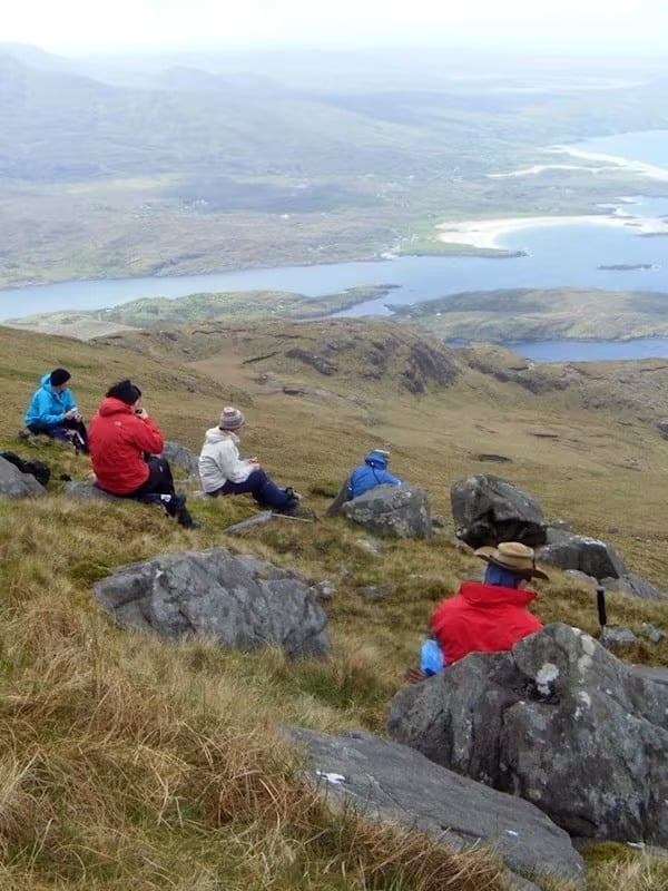 Group of people sitting on top of a mountain admiring the view